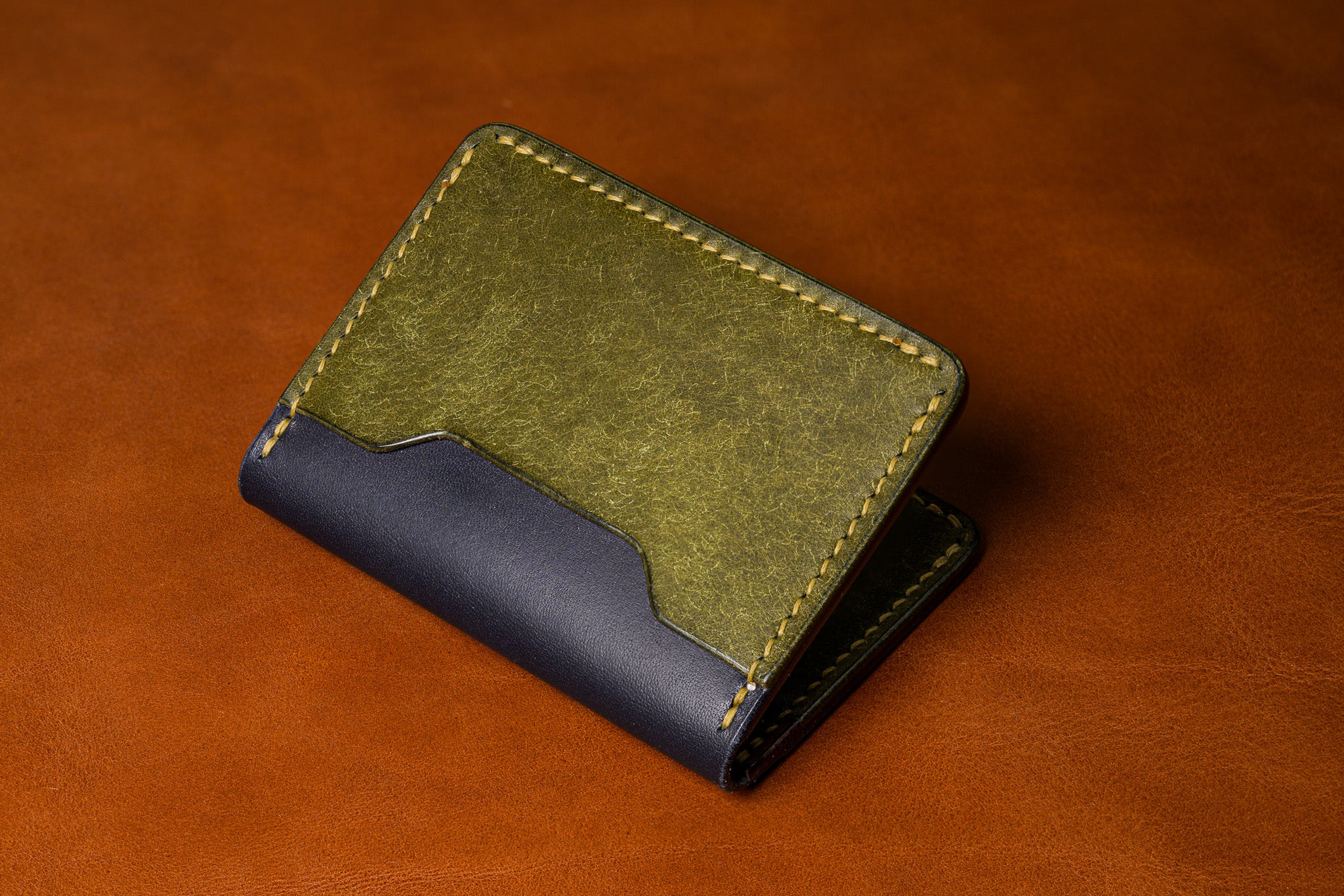 Two-tone leather wallet with green top section and black bottom section on a brown background