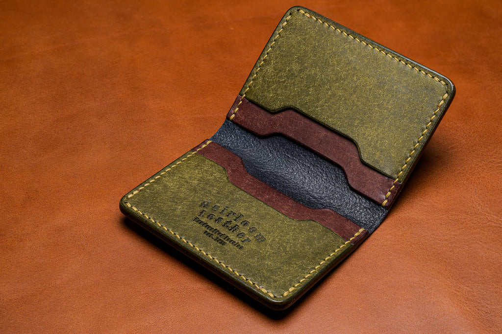 Green leather wallet with brown accents on a brown leather background