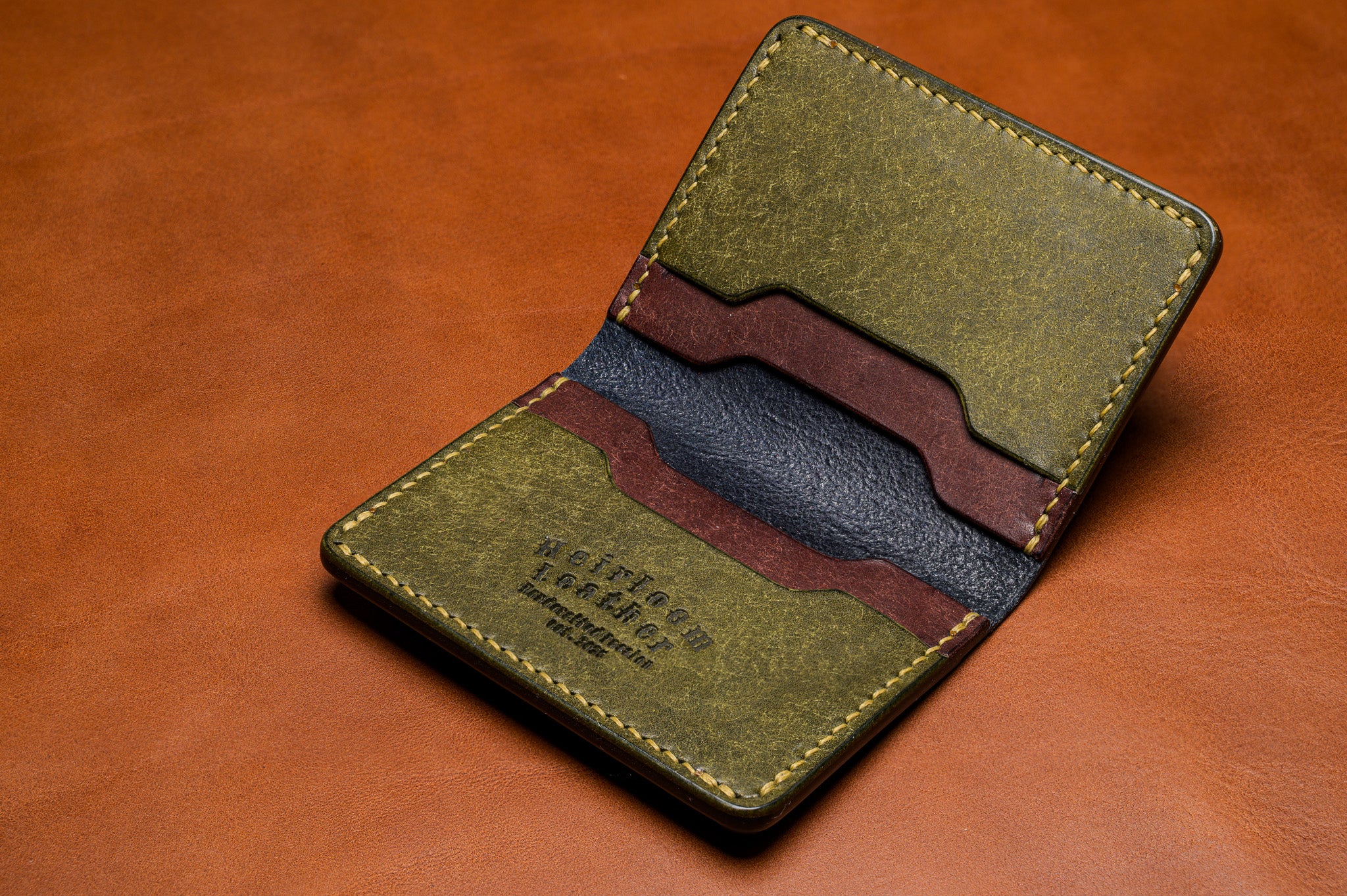 Green leather wallet with brown accents on a brown leather background