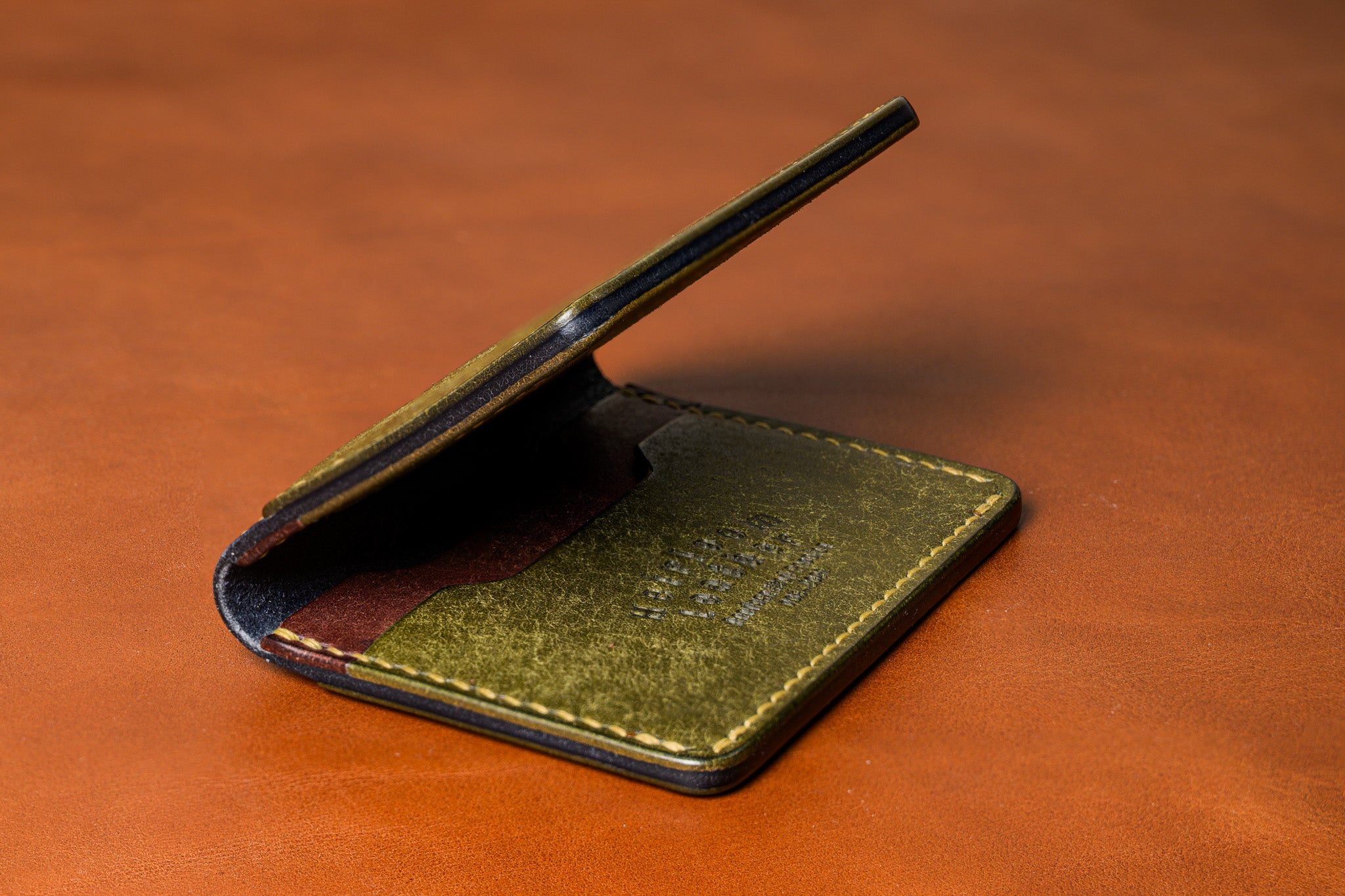 Green leather wallet on a brown leather surface