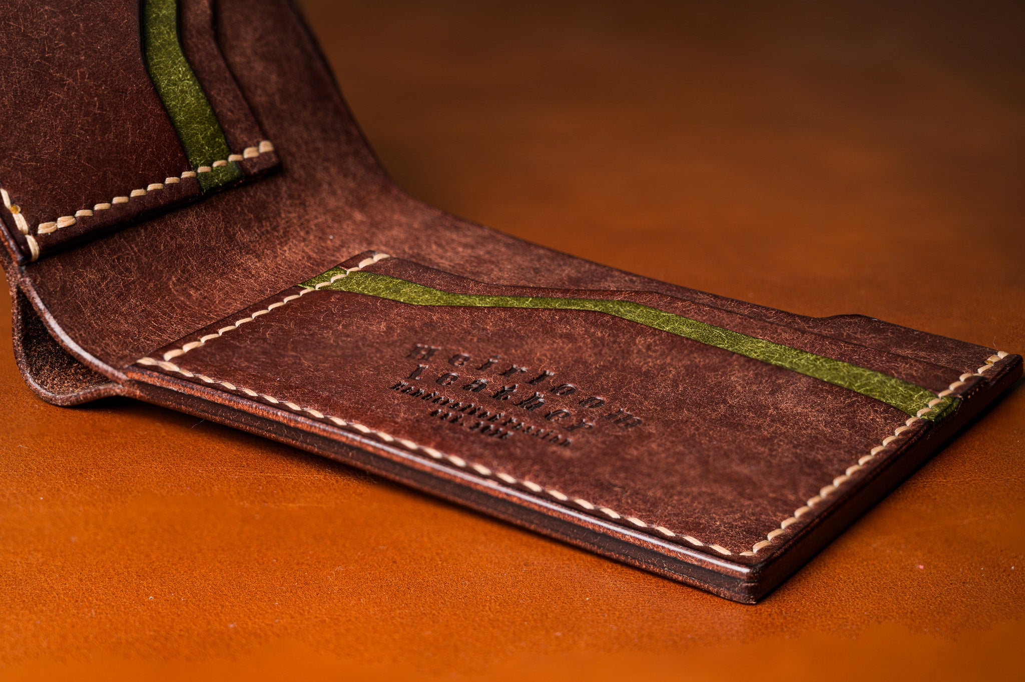 Brown leather wallet with green stitching on a brown background