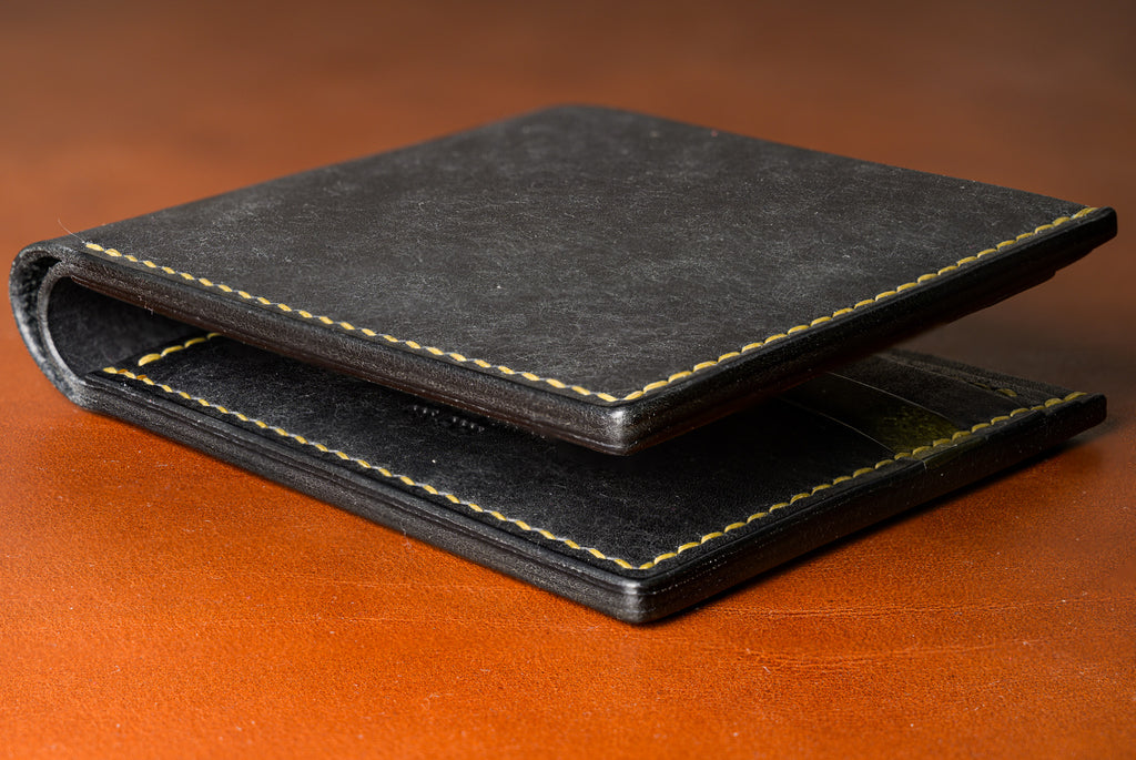 Black leather wallet with gold stitching on a brown surface