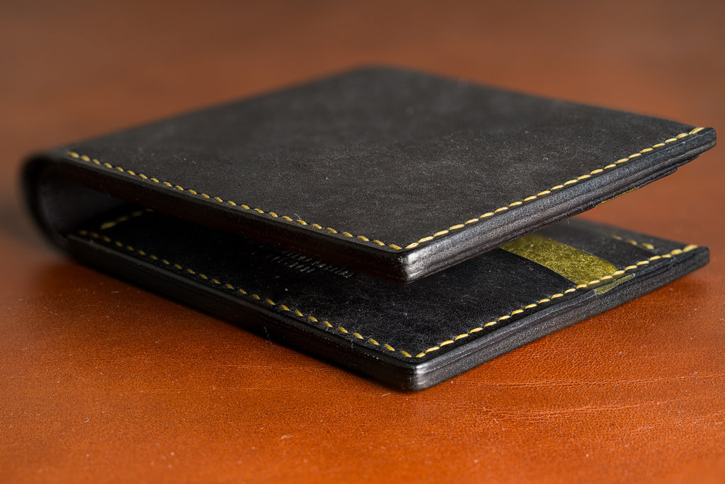 Black leather wallet with gold stitching on a brown surface