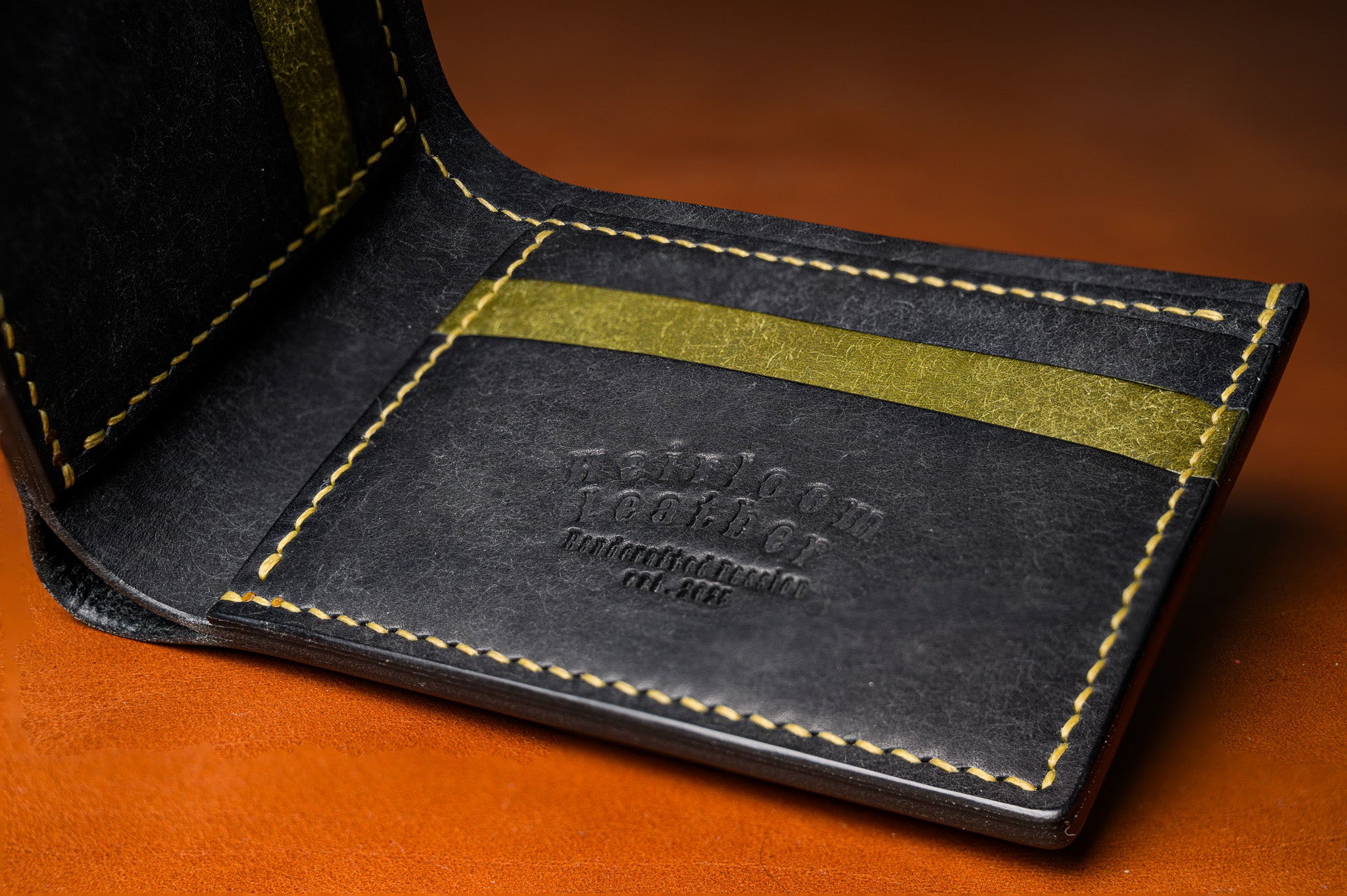 Close-up of a black leather wallet with gold stitching on a brown background