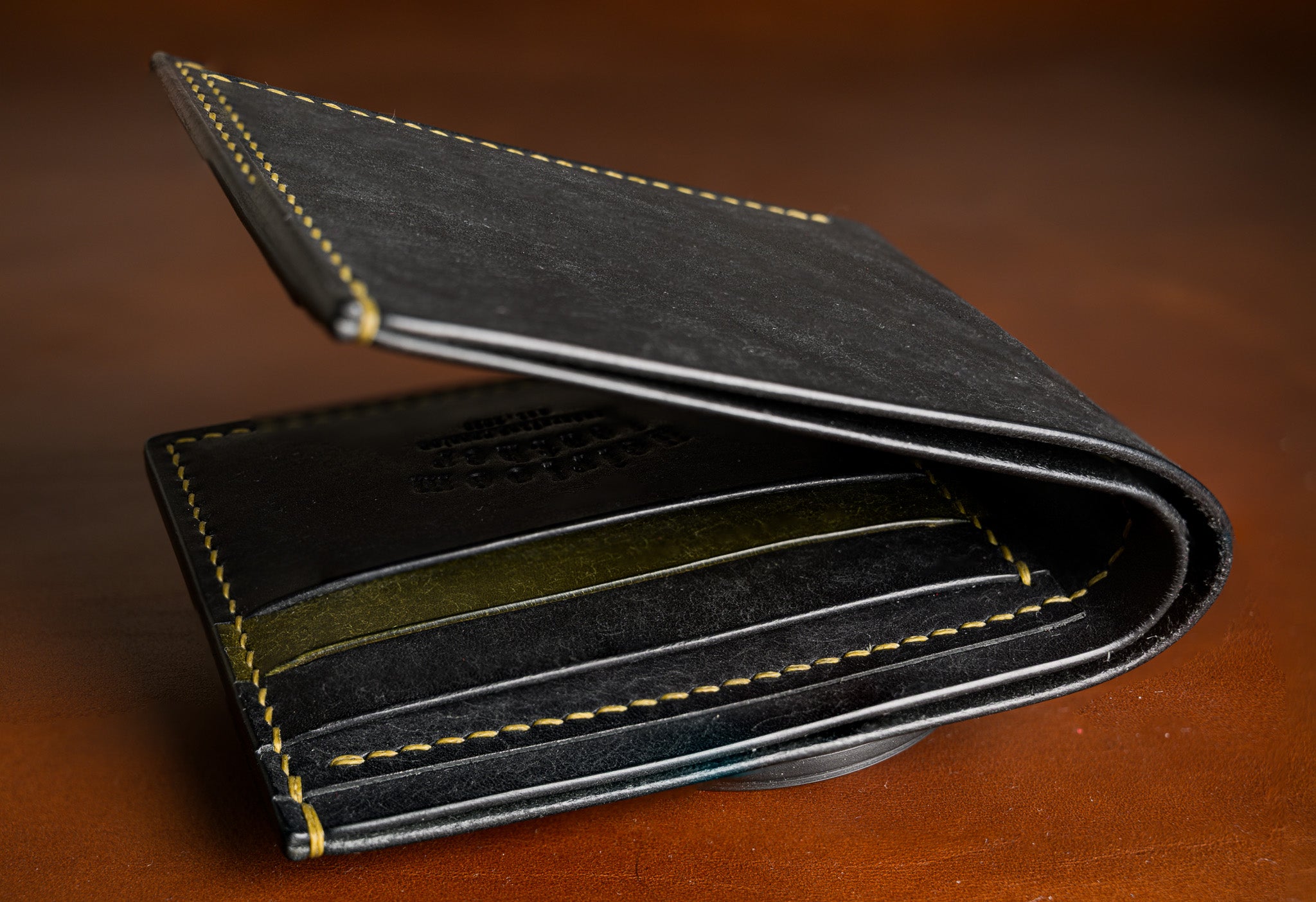 Black leather wallet with yellow stitching on a wooden surface