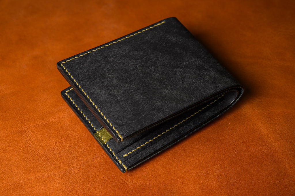 Black leather wallet with gold stitching on a brown leather background