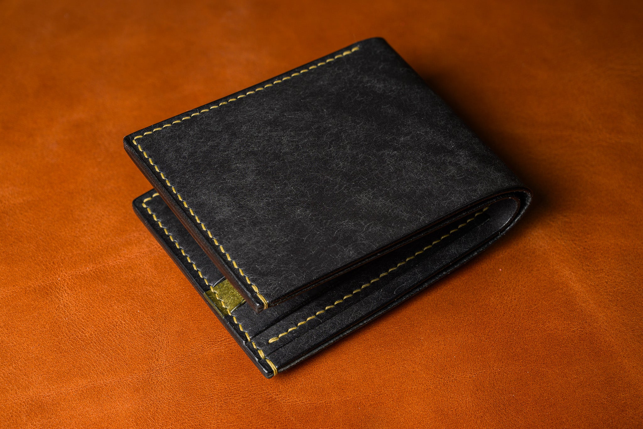 Black leather wallet with gold stitching on a brown leather background