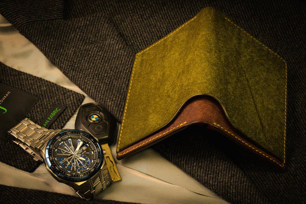 Gold watch, car key, and green wallet on a textured surface