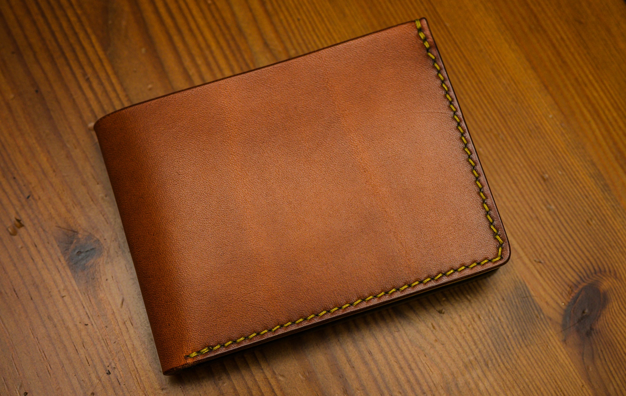 Brown leather wallet with gold stitching on a wooden surface