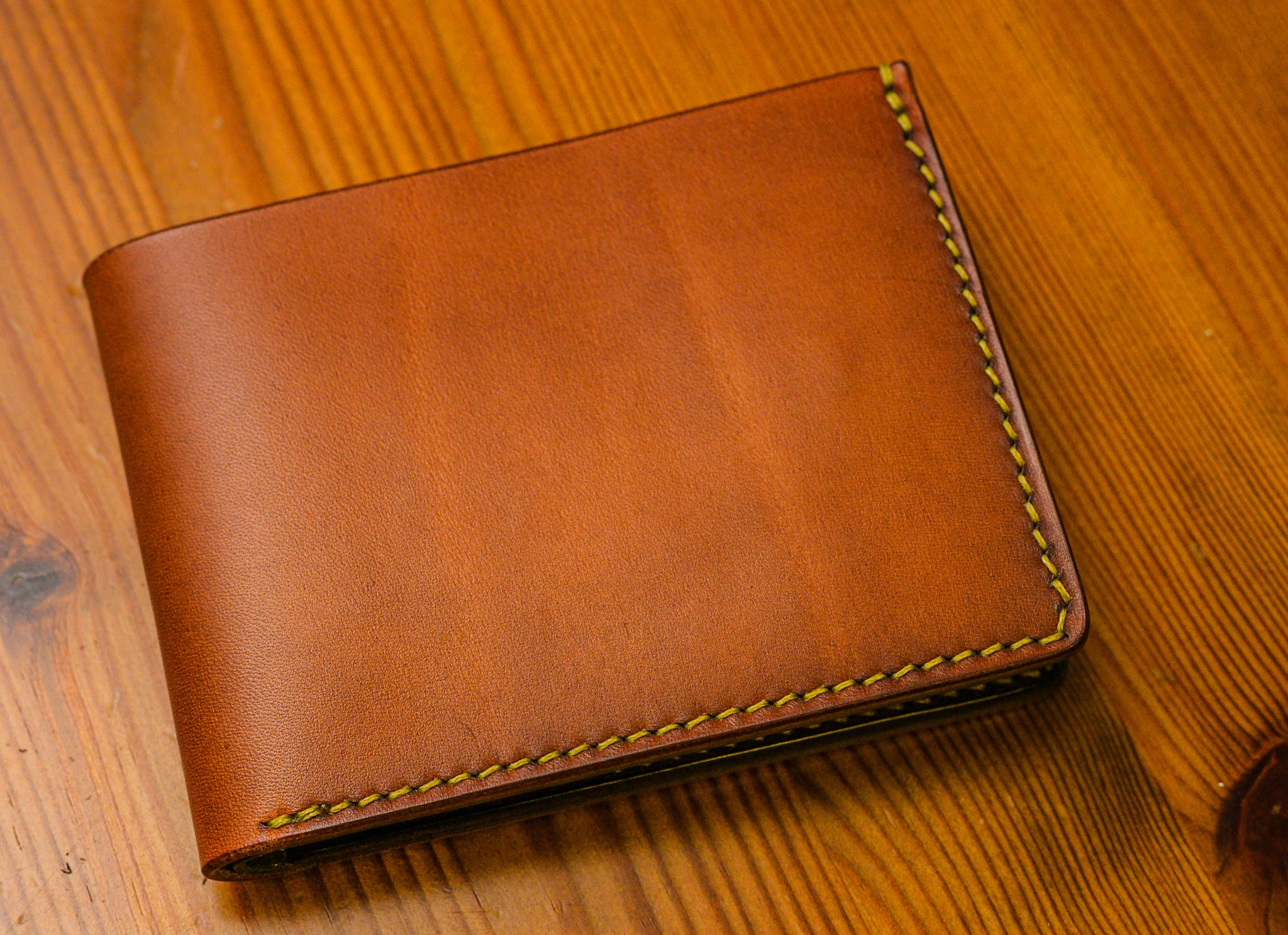 Brown leather wallet with yellow stitching on a wooden surface