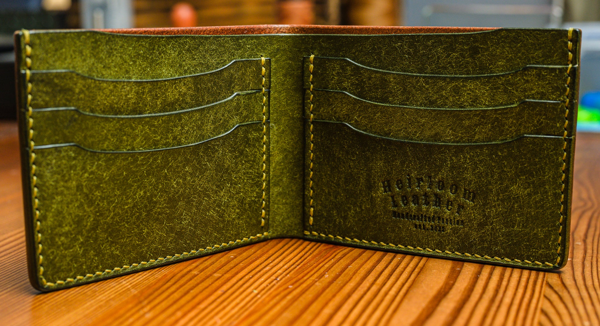 Green leather wallet with visible branding on a wooden surface