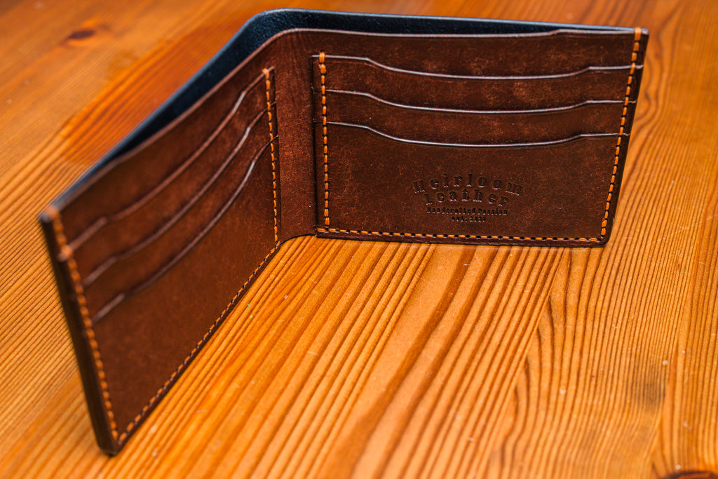 Navy and Tobacco leather wallet with stitching detail on a wooden surface