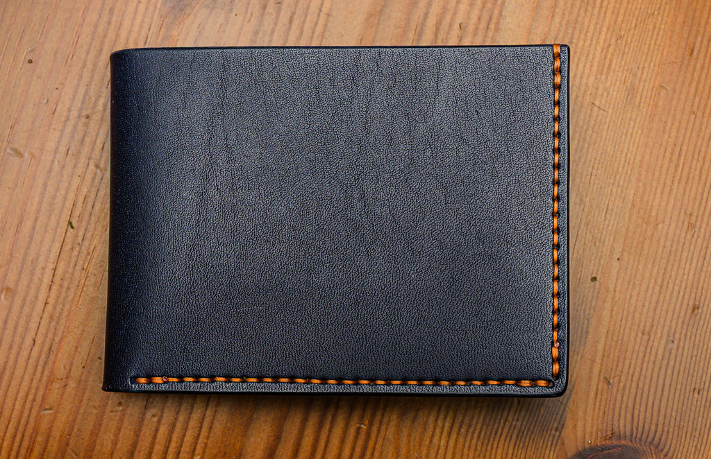 Navy leather wallet with brown stitching on a wooden surface