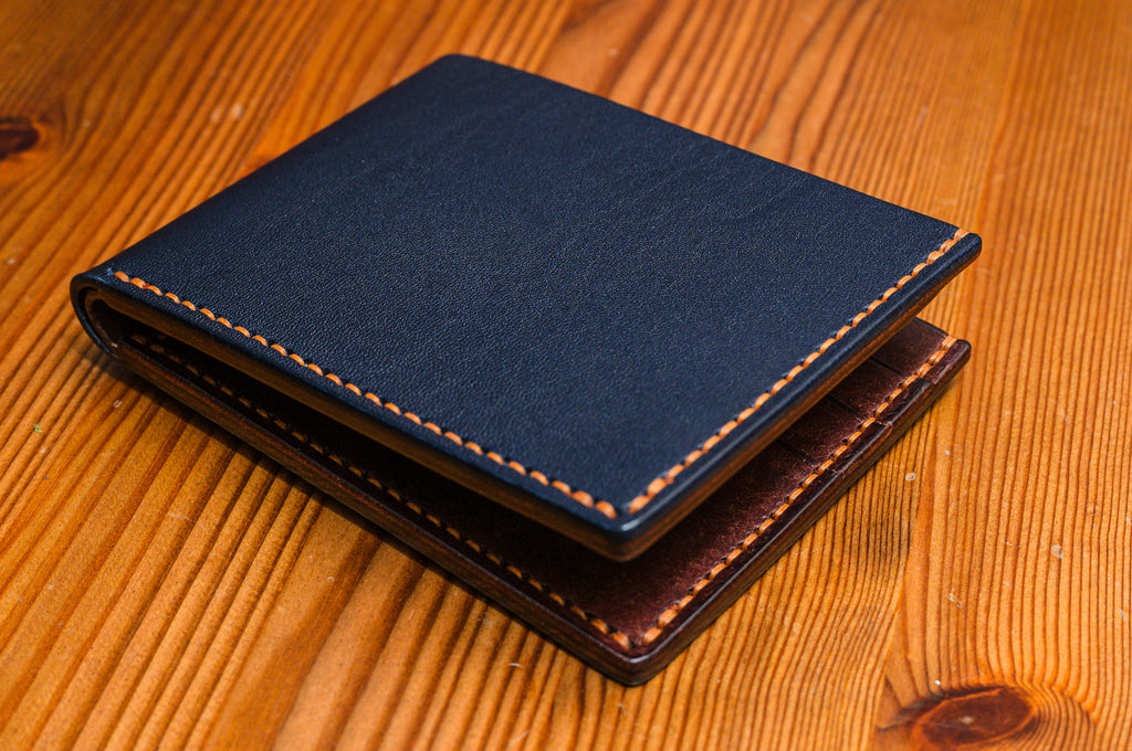 Two tone leather wallet in Navy and Tobacco colour on a wooden surface.