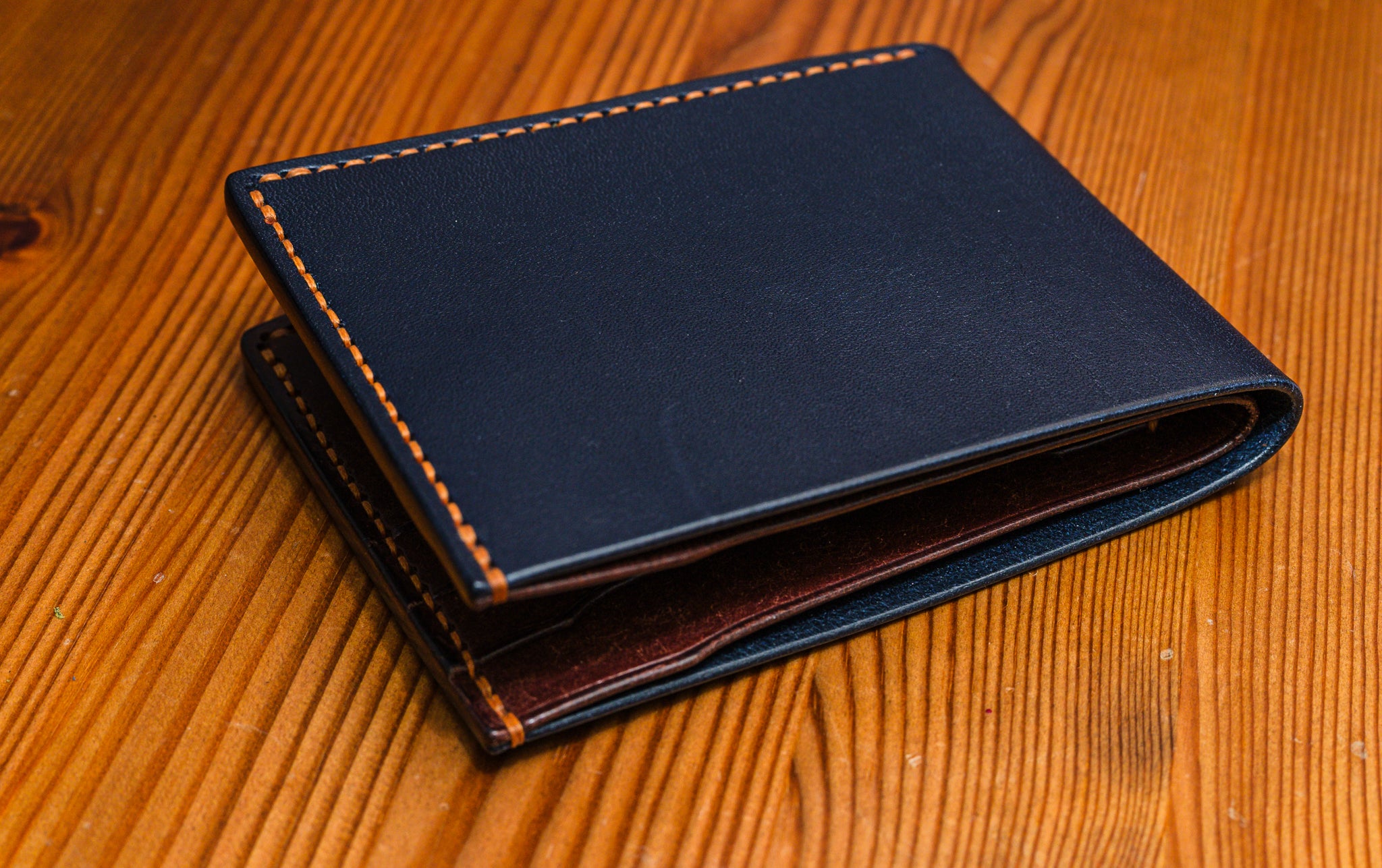 Two tone leather wallet in Navy and Tobacco colour on a wooden surface.