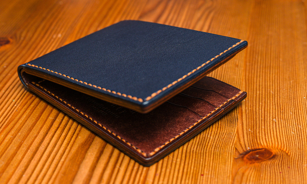 Two tone leather wallet in Navy and Tobacco colour on a wooden surface.