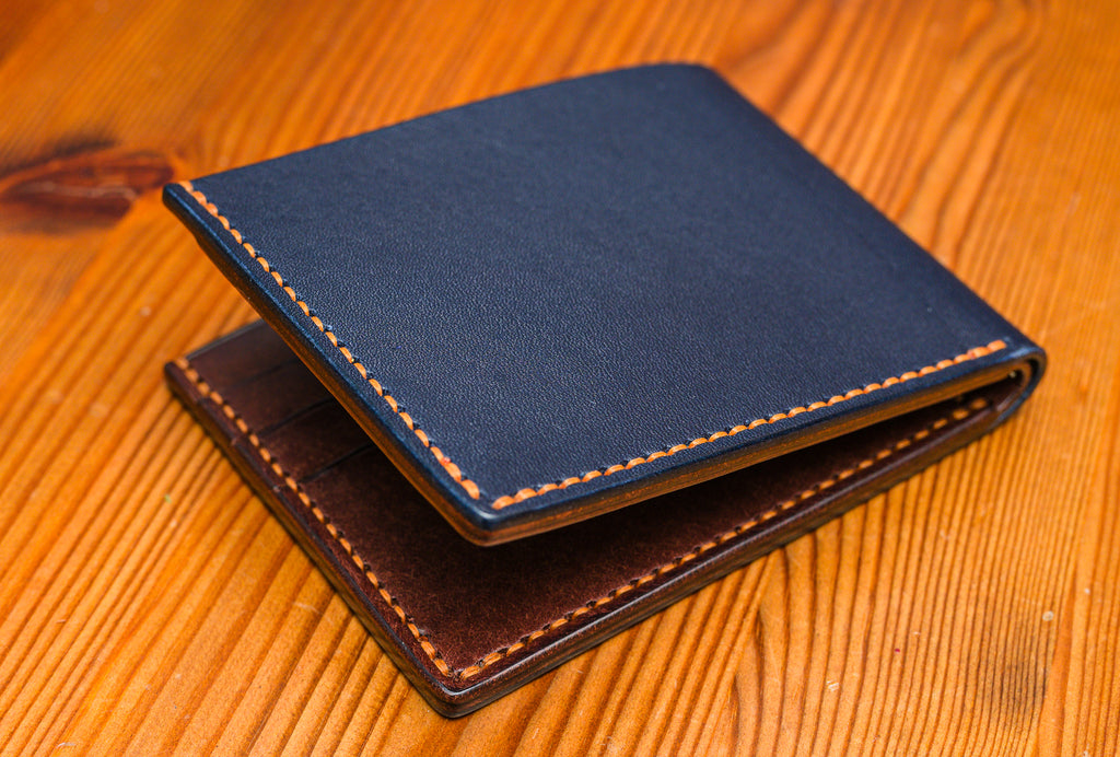 Two tone leather wallet in Navy and Tobacco colour on a wooden surface.