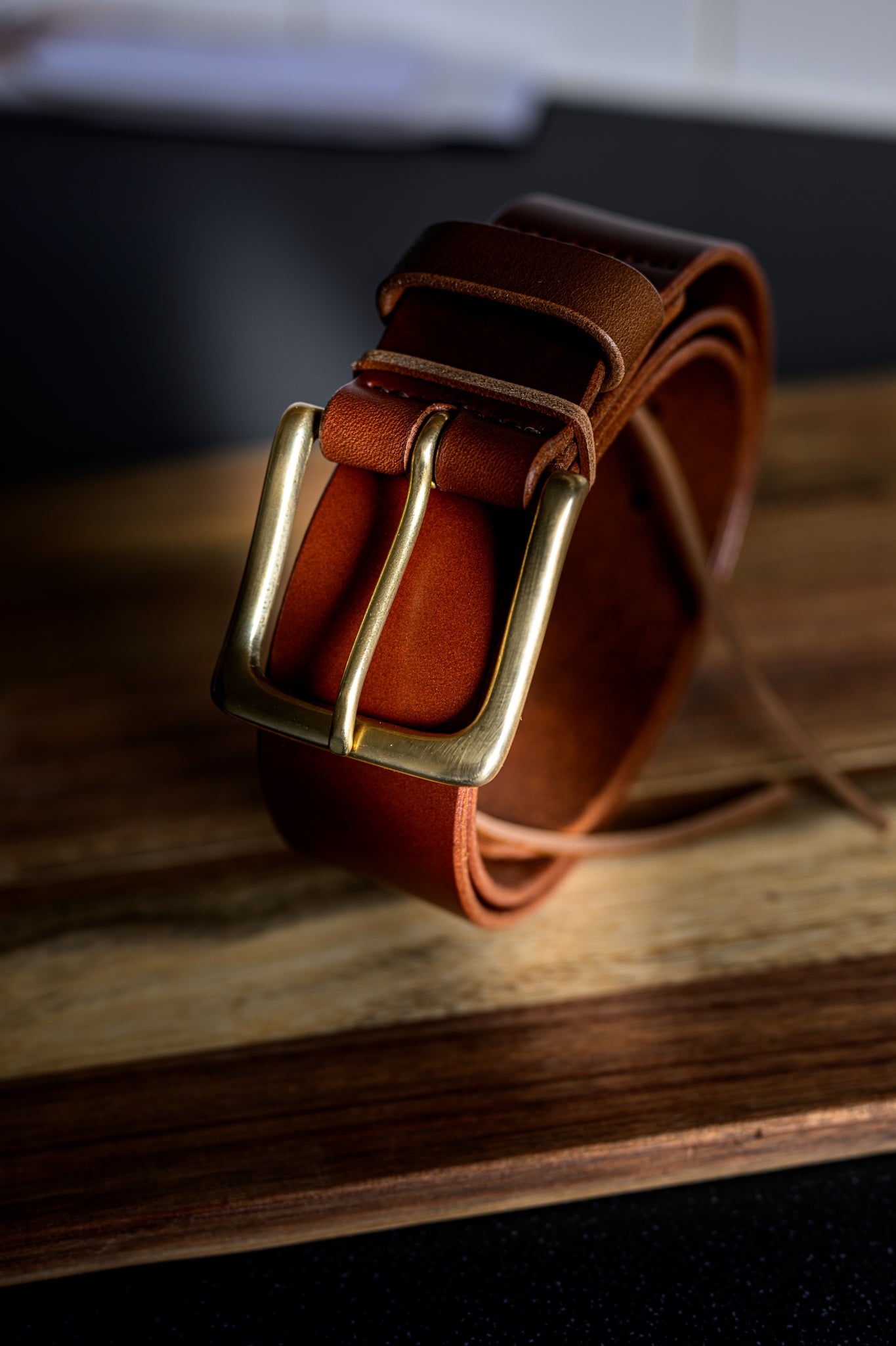 Brown leather belt with a gold buckle on a wooden surface