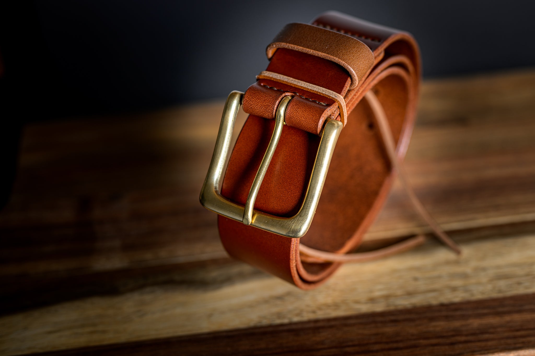 Brown leather belt with a gold buckle on a wooden surface