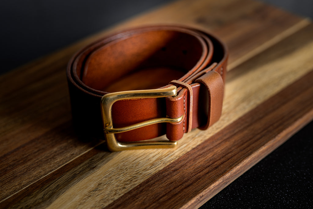 Brown leather belt with a gold buckle on a wooden surface