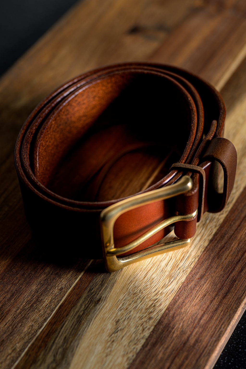 Brown leather belt with a gold buckle on a wooden surface