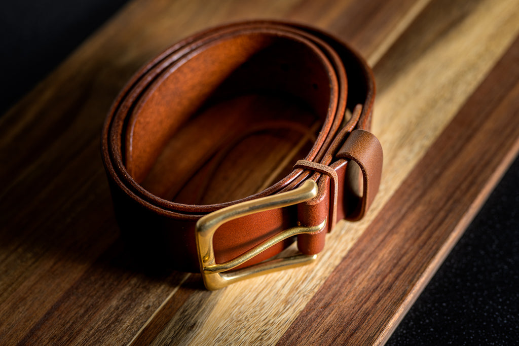 Brown leather belt with a gold buckle on a wooden surface
