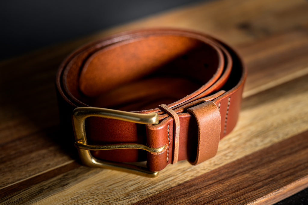 Brown leather belt with a gold buckle on a wooden surface