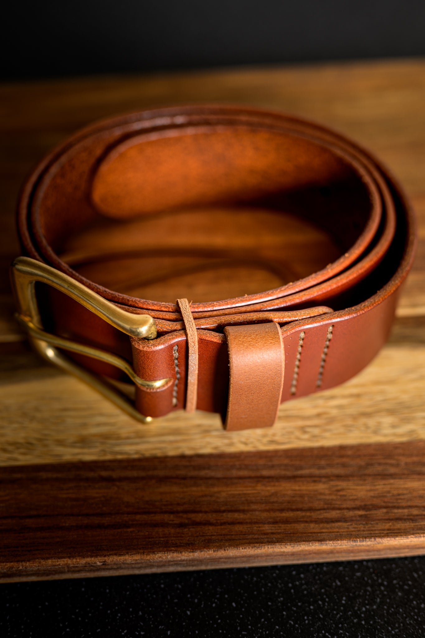 Brown leather belt with brass buckle on a wooden surface