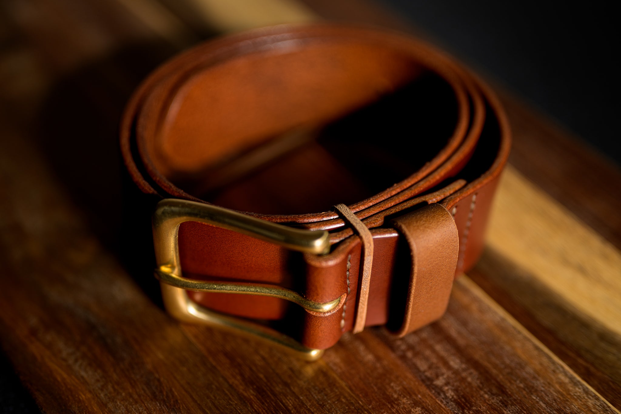 Brown leather belt with a gold buckle on a wooden surface