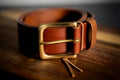 Brown leather belt with a gold buckle on a wooden surface