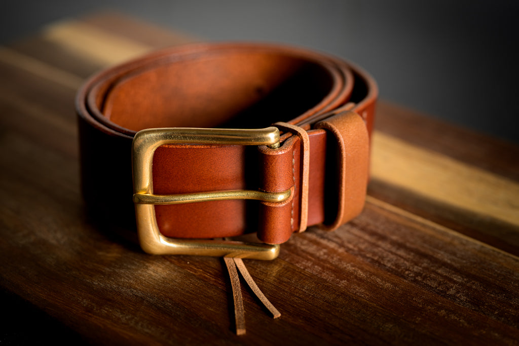 Brown leather belt with a gold buckle on a wooden surface