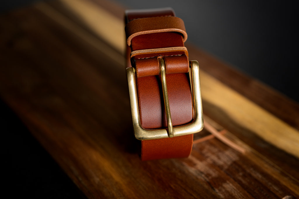 Brown leather belt with a gold buckle on a wooden surface
