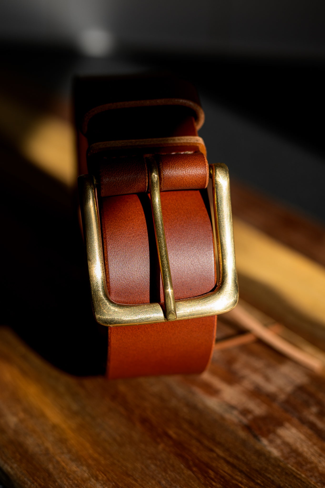 Brown leather belt with brass buckle on a wooden surface