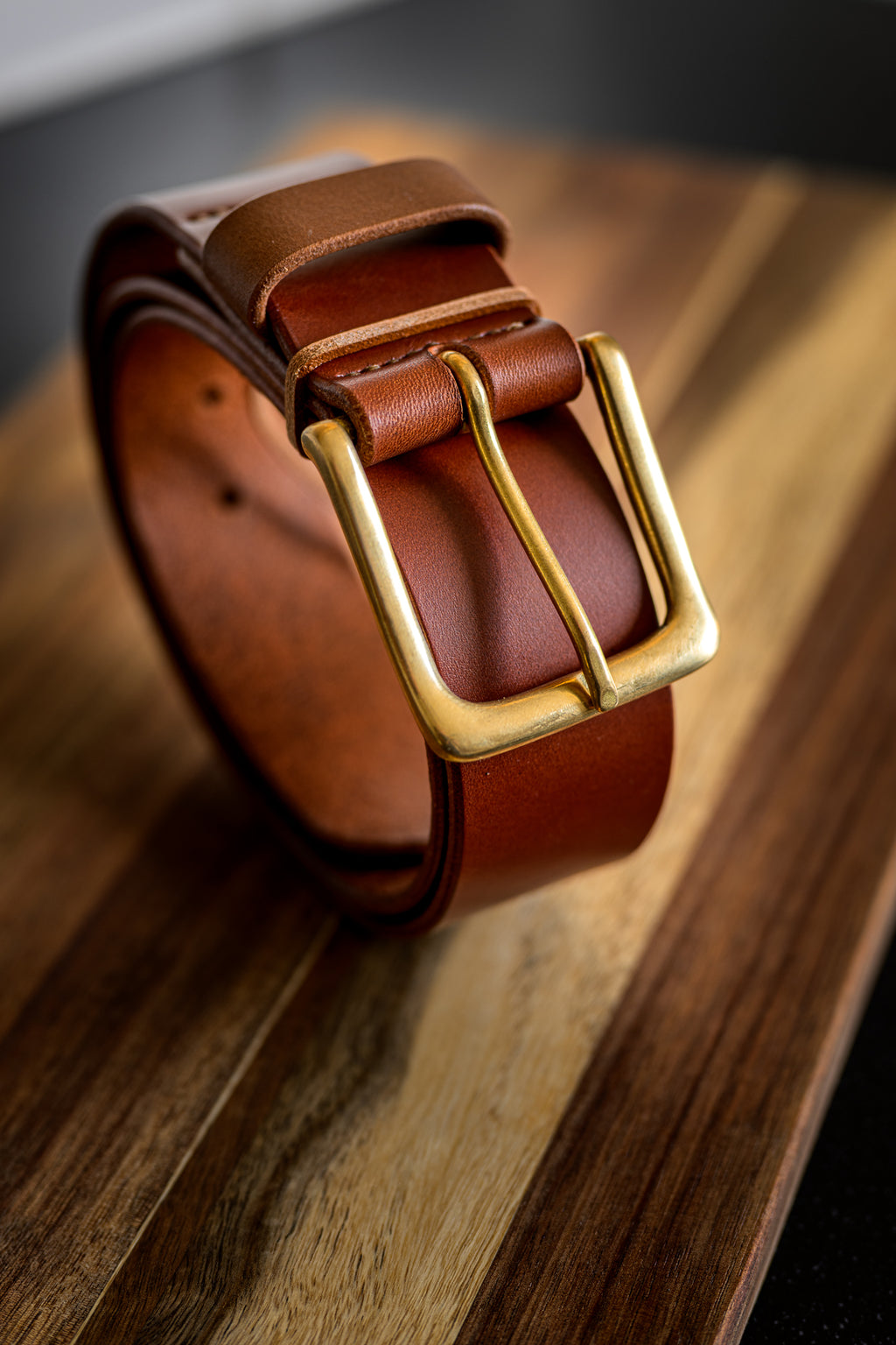 Brown leather belt with a gold buckle on a wooden surface