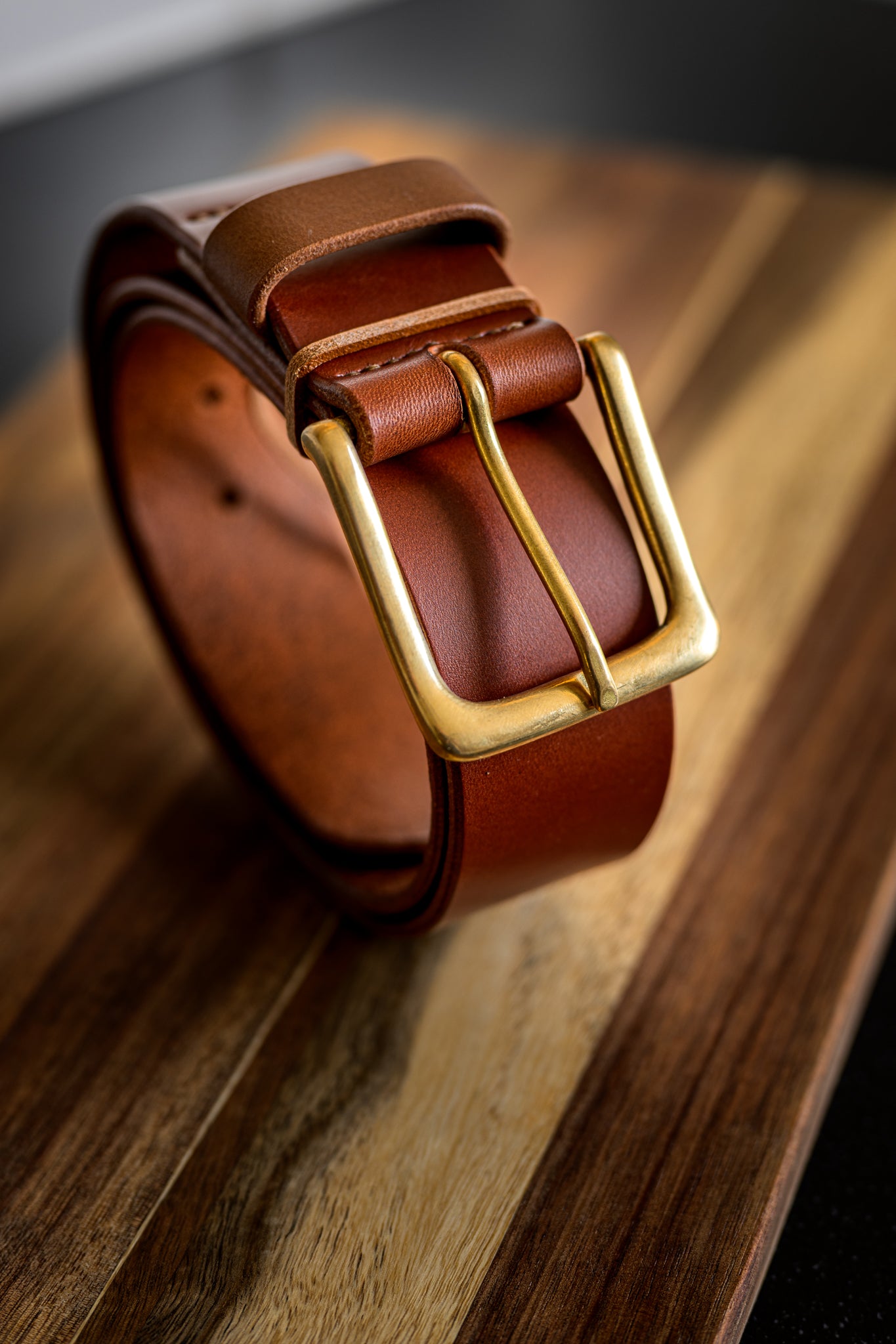 Brown leather belt with a gold buckle on a wooden surface