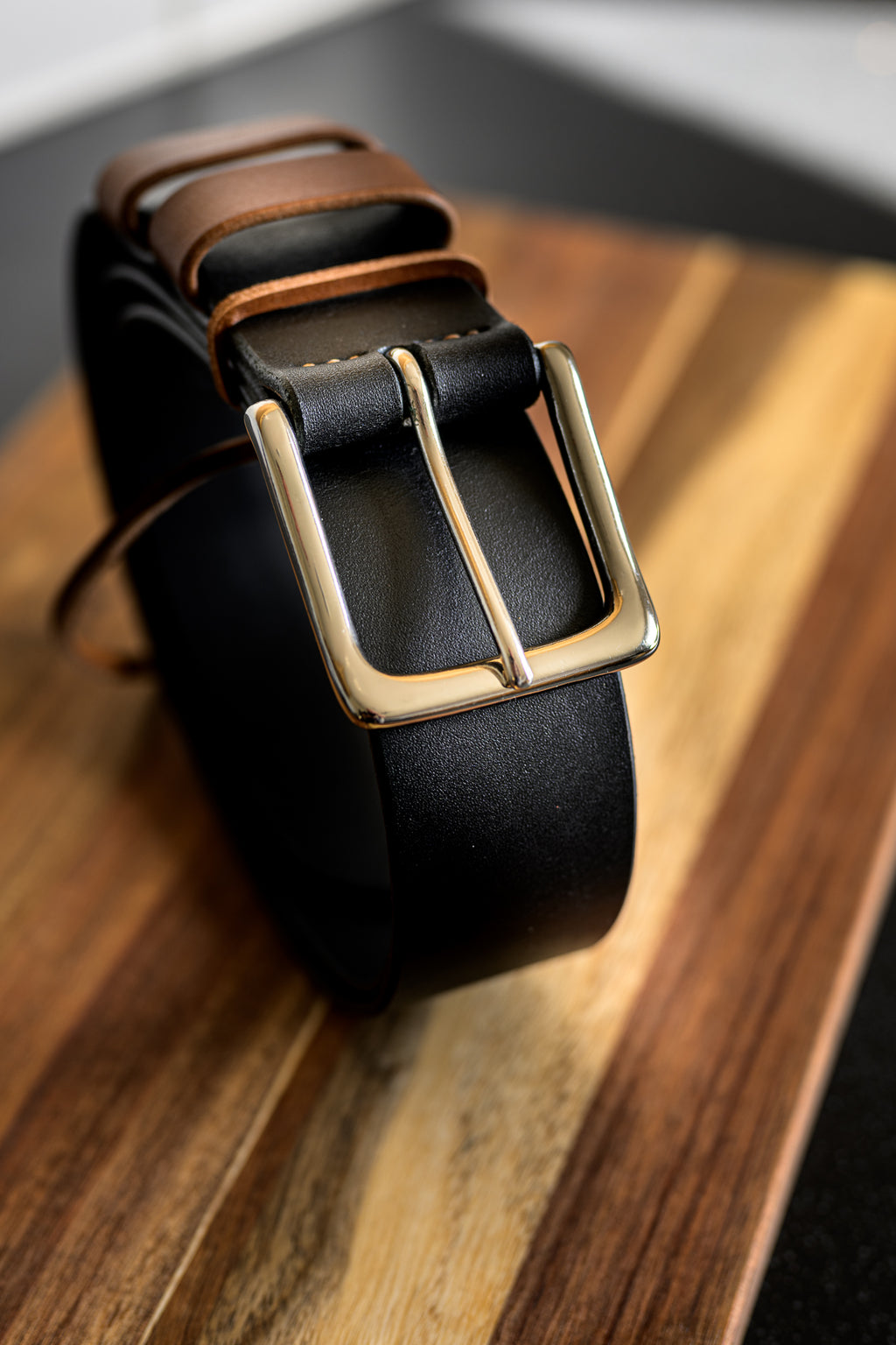 Black leather belt with a gold buckle on a wooden surface