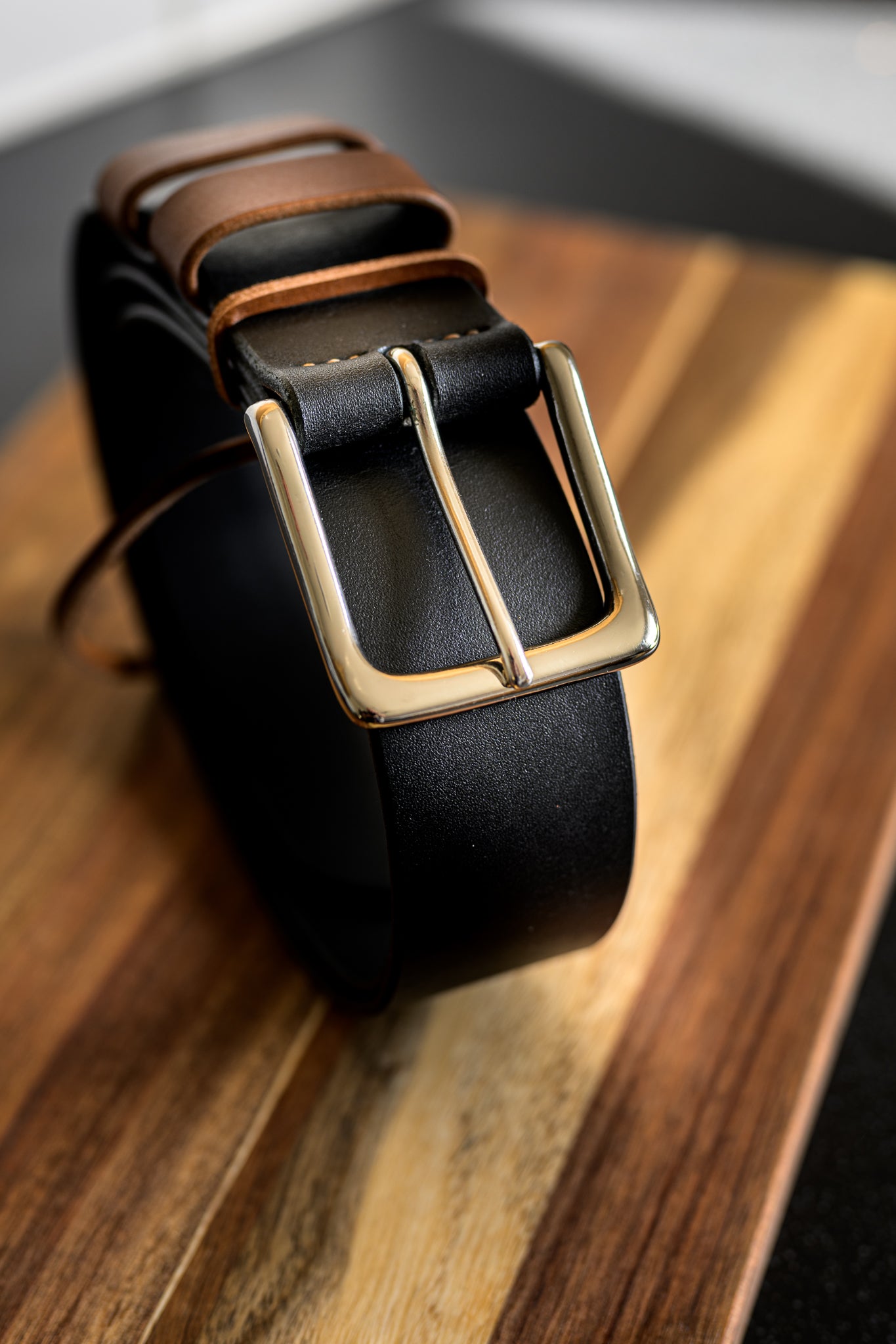 Black leather belt with a gold buckle on a wooden surface