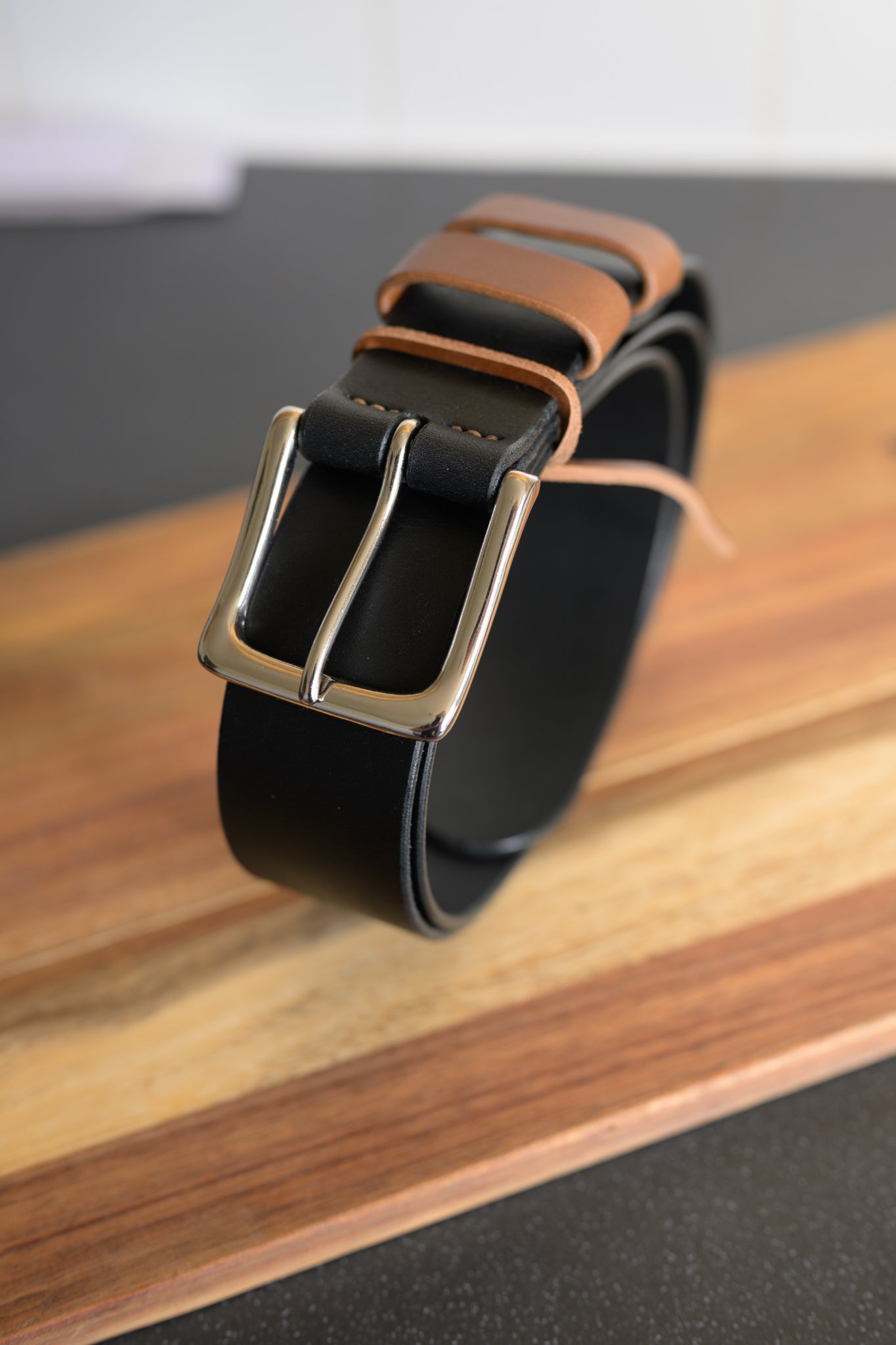 Black leather belt with a gold buckle on a wooden surface