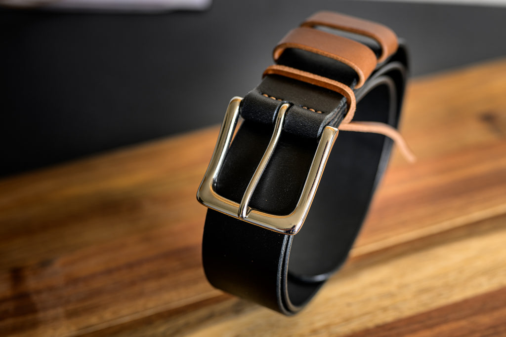 Black leather belt with a gold buckle on a wooden surface
