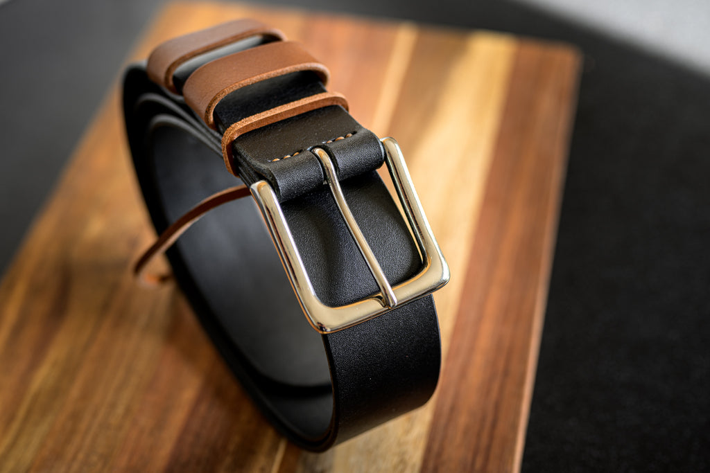 Black leather belt with a gold buckle on a wooden surface