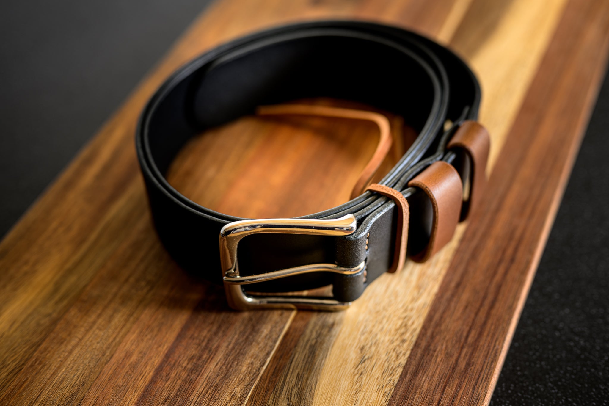 Black leather belt with a gold buckle on a wooden surface