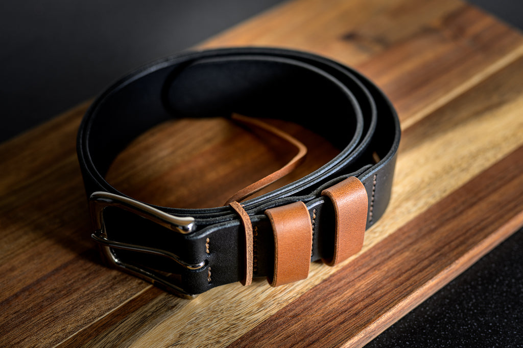 Black leather belt with brown accents on a wooden surface